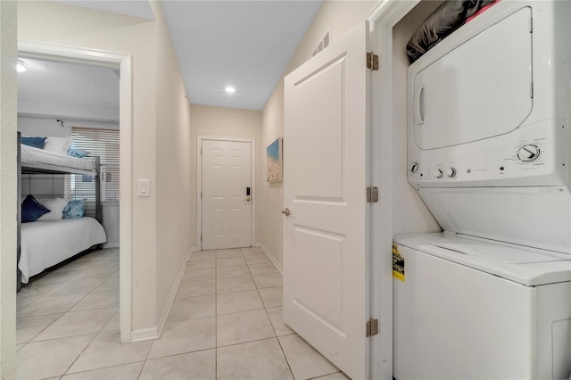 laundry area featuring light tile patterned floors, stacked washer and dryer, visible vents, laundry area, and baseboards