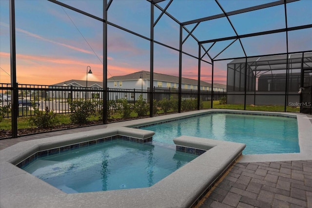 pool at dusk featuring a lanai and an in ground hot tub