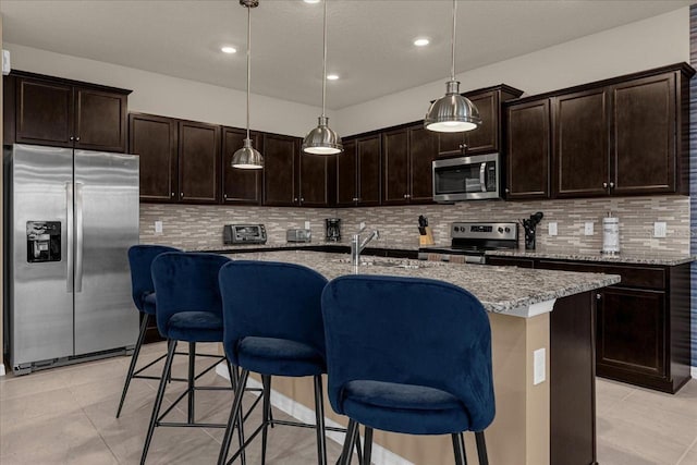 kitchen with tasteful backsplash, an island with sink, light stone counters, and stainless steel appliances