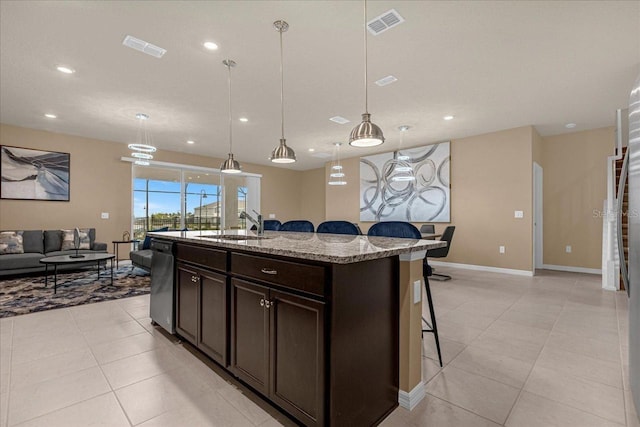 kitchen with a kitchen island with sink, decorative light fixtures, dishwasher, sink, and light stone countertops