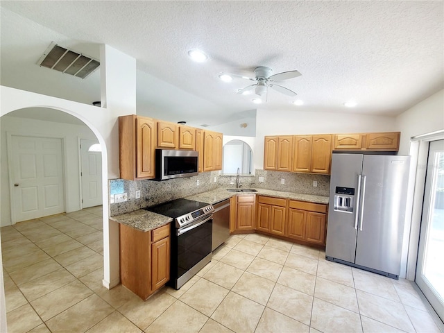 kitchen featuring light stone counters, stainless steel appliances, lofted ceiling, backsplash, and a sink