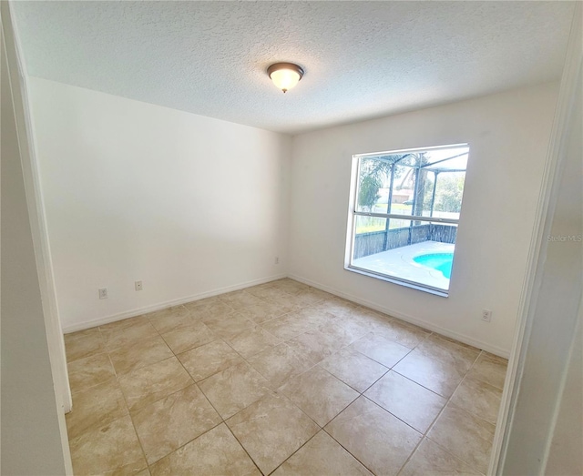 spare room featuring a textured ceiling, light tile patterned floors, and baseboards