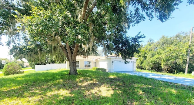 view of property hidden behind natural elements with a front lawn, fence, driveway, and an attached garage