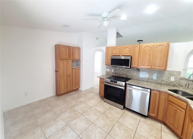 kitchen featuring arched walkways, tasteful backsplash, appliances with stainless steel finishes, a sink, and light stone countertops