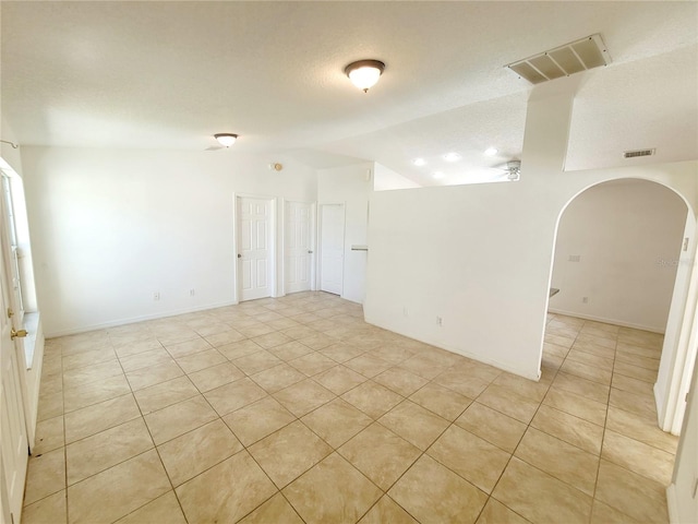 spare room featuring lofted ceiling, visible vents, arched walkways, and a textured ceiling