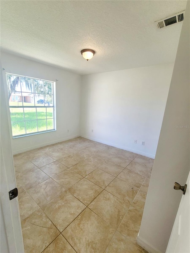 empty room with a textured ceiling, light tile patterned flooring, visible vents, and baseboards