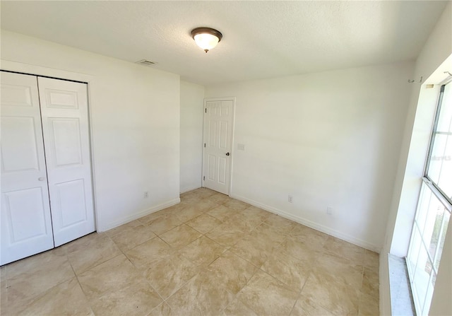 unfurnished bedroom featuring a closet, visible vents, a textured ceiling, and baseboards