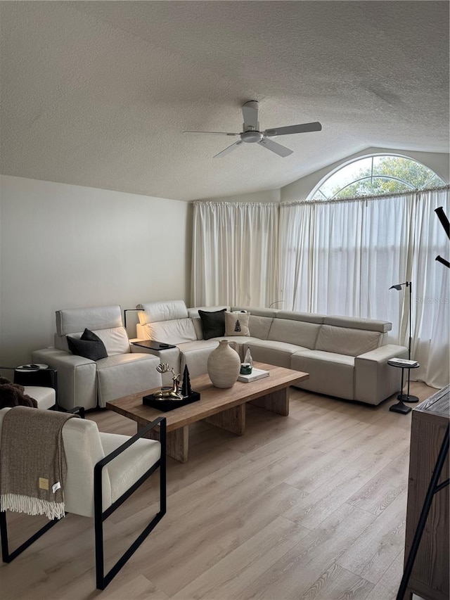 living room featuring a textured ceiling, ceiling fan, light hardwood / wood-style floors, and vaulted ceiling