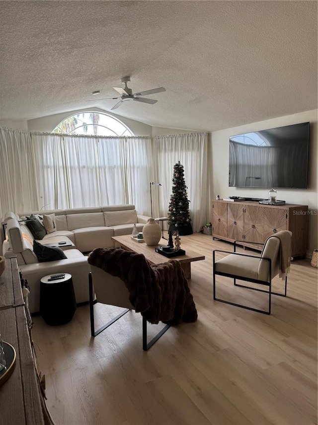 living room with a textured ceiling, ceiling fan, light hardwood / wood-style floors, and vaulted ceiling