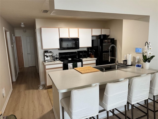 kitchen with a breakfast bar, black appliances, sink, light hardwood / wood-style floors, and kitchen peninsula