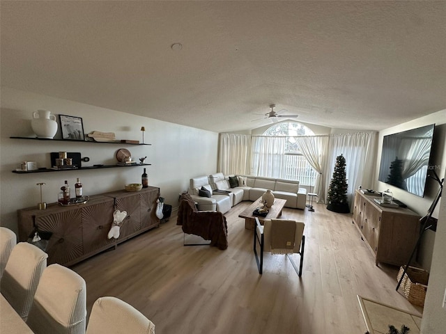 living room featuring a textured ceiling, light wood-type flooring, vaulted ceiling, and ceiling fan