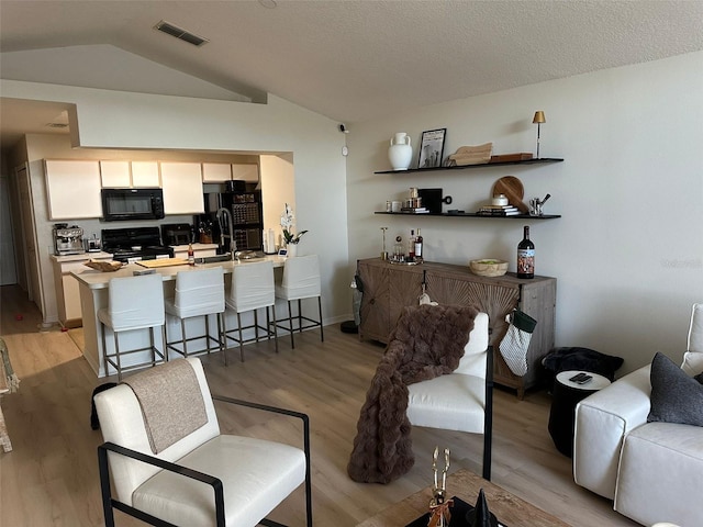 living room featuring a textured ceiling, sink, light hardwood / wood-style floors, and lofted ceiling