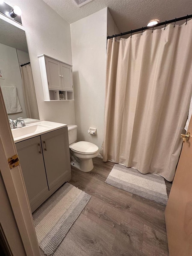 bathroom with vanity, toilet, wood-type flooring, and a textured ceiling