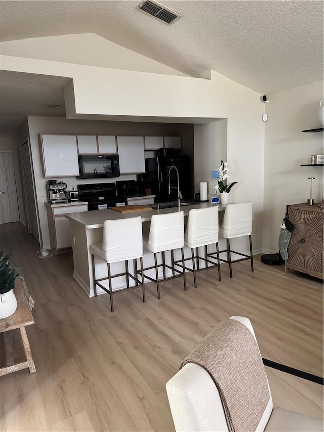 kitchen featuring black appliances, kitchen peninsula, a breakfast bar area, and vaulted ceiling