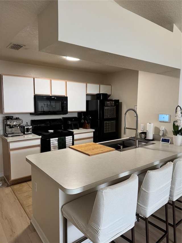 kitchen with a kitchen breakfast bar, white cabinetry, black appliances, and light hardwood / wood-style floors