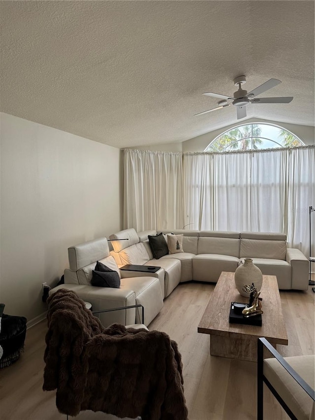 living room with a textured ceiling, ceiling fan, vaulted ceiling, and light wood-type flooring