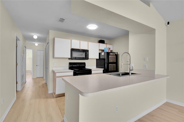 kitchen featuring light wood finished floors, a peninsula, a sink, visible vents, and black appliances