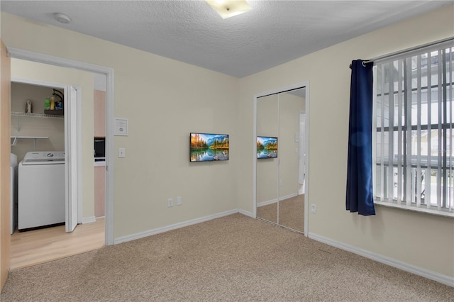 unfurnished bedroom featuring baseboards, carpet floors, a textured ceiling, and washer / dryer