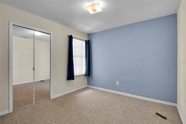 unfurnished bedroom featuring carpet flooring, a textured ceiling, visible vents, and a closet