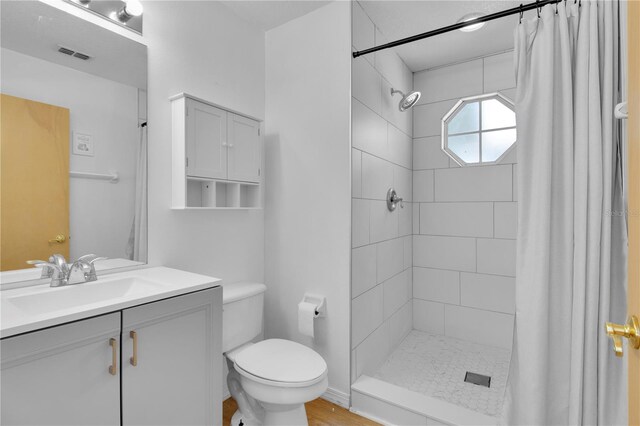 bathroom featuring visible vents, vanity, a tile shower, and toilet