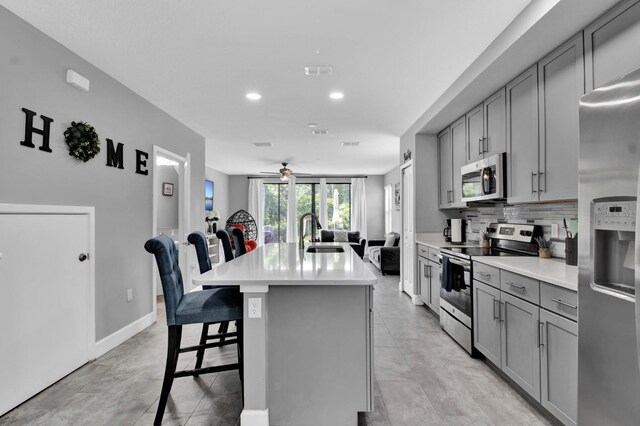 kitchen featuring a kitchen bar, light tile patterned floors, ceiling fan, appliances with stainless steel finishes, and a center island with sink