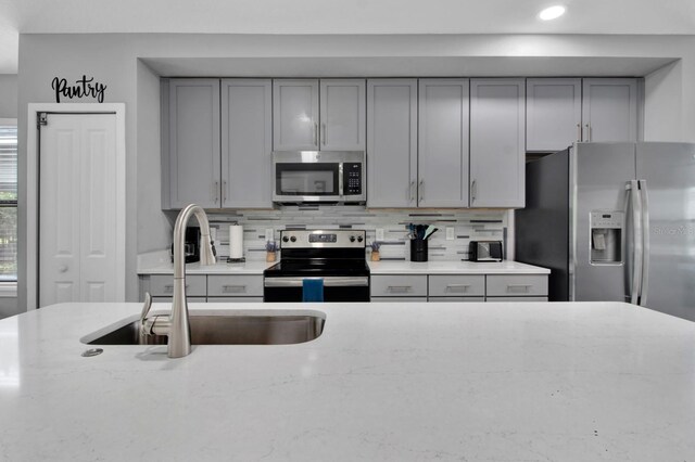 kitchen featuring gray cabinetry, light stone countertops, stainless steel appliances, sink, and decorative backsplash