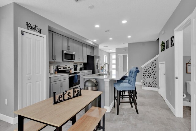 kitchen featuring a kitchen breakfast bar, light tile patterned floors, appliances with stainless steel finishes, gray cabinets, and decorative backsplash