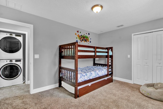 carpeted bedroom with a textured ceiling and stacked washing maching and dryer