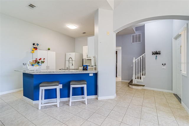 kitchen featuring light tile patterned floors, light stone counters, white cabinetry, kitchen peninsula, and a kitchen breakfast bar