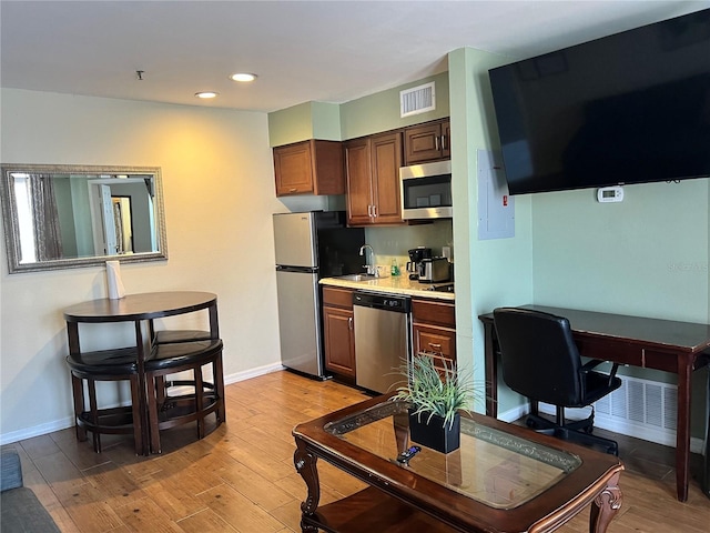 kitchen with appliances with stainless steel finishes, sink, and light hardwood / wood-style flooring