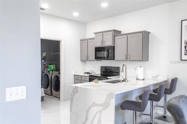 kitchen with light tile patterned floors, washer and dryer, black appliances, light stone counters, and gray cabinetry