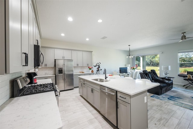 kitchen with an island with sink, stainless steel appliances, ceiling fan, and light hardwood / wood-style floors