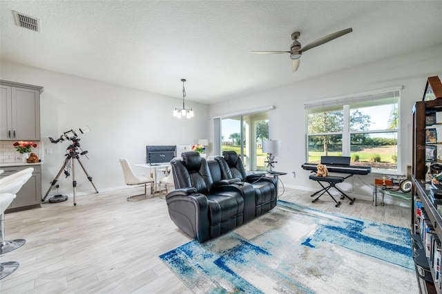 living room with ceiling fan with notable chandelier, a textured ceiling, and light hardwood / wood-style flooring