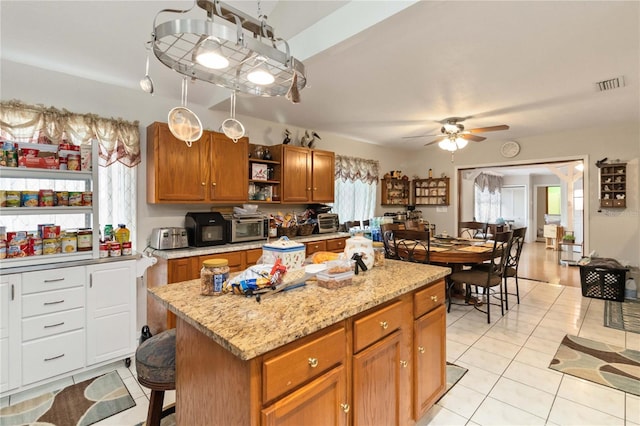 kitchen with light stone countertops, a breakfast bar, ceiling fan, light tile patterned floors, and a kitchen island