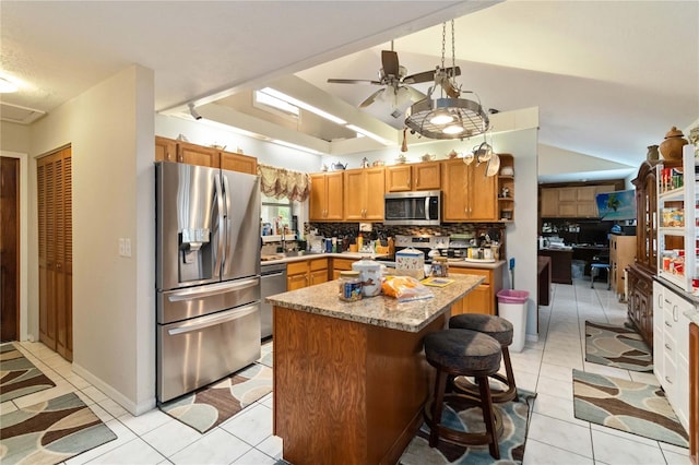 kitchen featuring ceiling fan, light tile patterned floors, decorative backsplash, a kitchen island, and appliances with stainless steel finishes