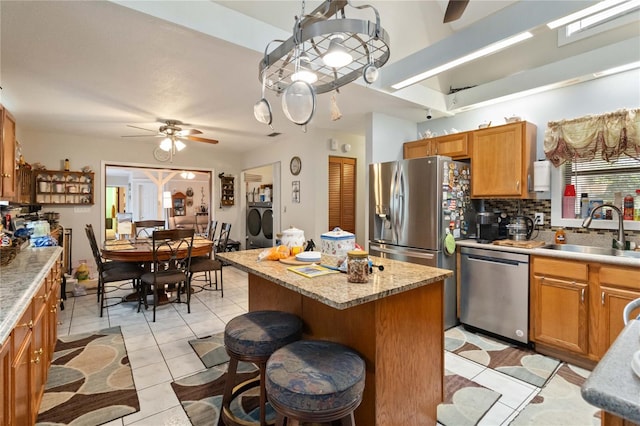 kitchen with ceiling fan, sink, tasteful backsplash, a kitchen island, and appliances with stainless steel finishes