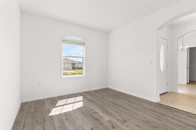 spare room featuring arched walkways, baseboards, and wood finished floors