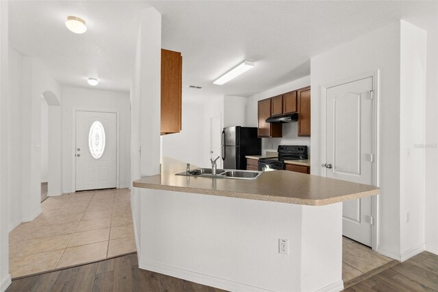 kitchen with black appliances, under cabinet range hood, a sink, light wood-style floors, and a peninsula