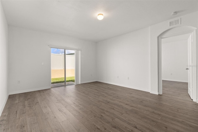 spare room with dark wood-style floors, visible vents, and baseboards