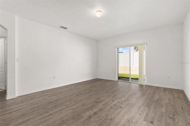 empty room with arched walkways, visible vents, baseboards, and wood finished floors