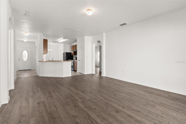 unfurnished living room with arched walkways, visible vents, and wood finished floors