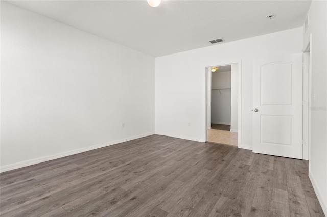 unfurnished bedroom featuring a spacious closet, visible vents, baseboards, wood finished floors, and a closet