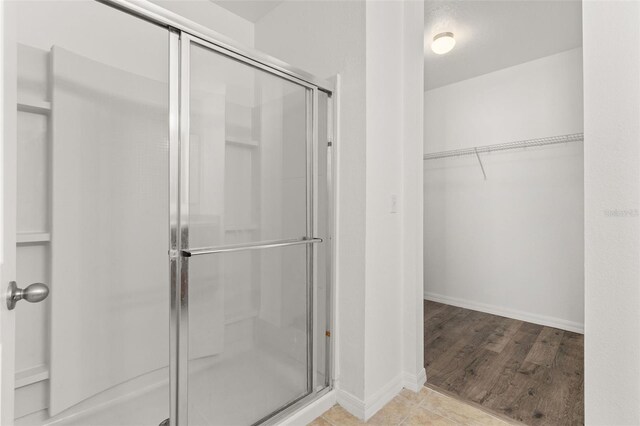 full bathroom with a shower stall, a spacious closet, wood finished floors, and baseboards