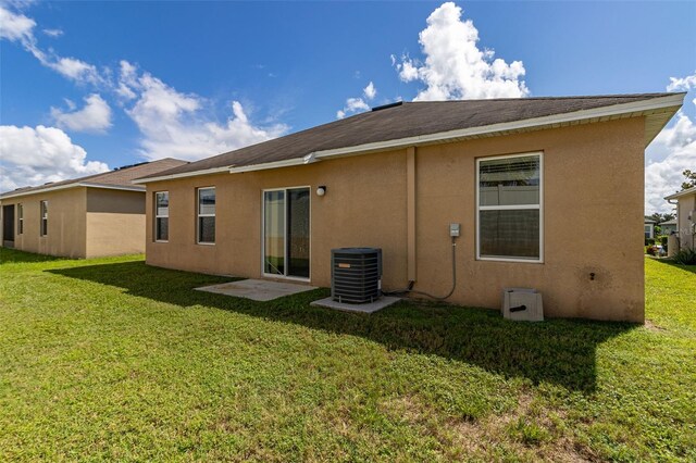 rear view of house with stucco siding, cooling unit, and a yard