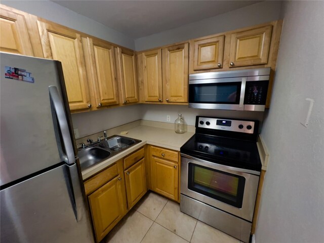 kitchen with appliances with stainless steel finishes, light countertops, a sink, and light tile patterned floors