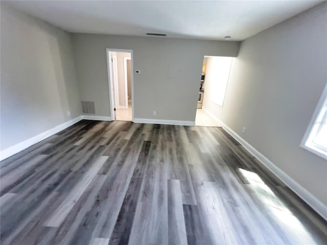 spare room featuring dark wood-type flooring, visible vents, and baseboards