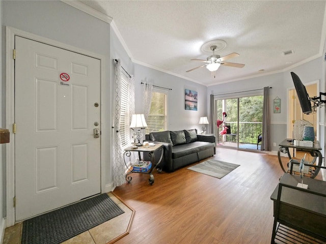 living room featuring ceiling fan, a textured ceiling, wood-type flooring, and ornamental molding