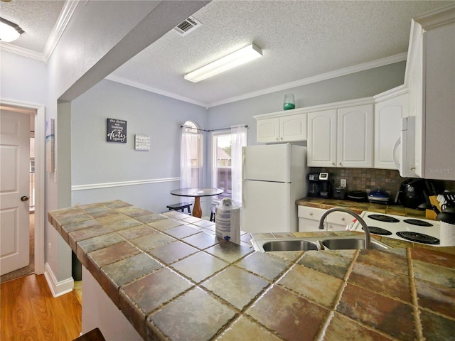 kitchen featuring light wood-type flooring, white appliances, sink, tile counters, and a textured ceiling