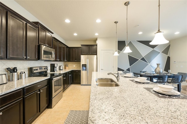 kitchen featuring backsplash, light stone counters, sink, hanging light fixtures, and appliances with stainless steel finishes