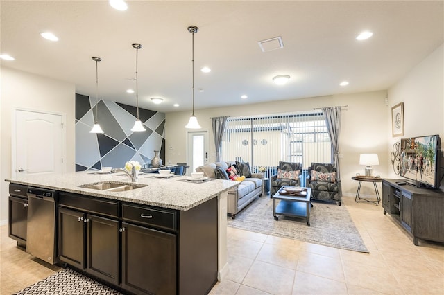 kitchen featuring decorative light fixtures, a center island with sink, stainless steel dishwasher, sink, and light stone counters